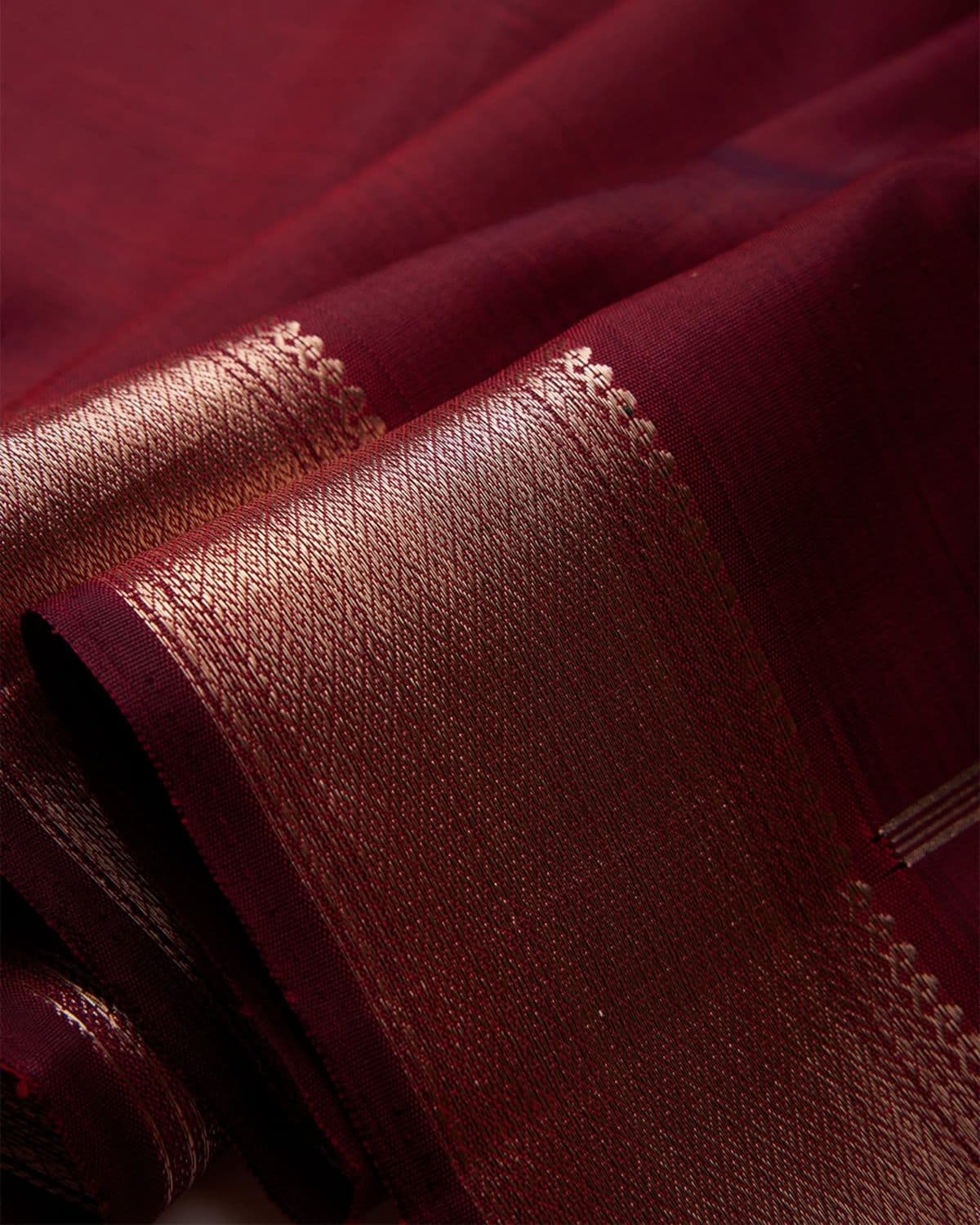 Macro detail of deep maroon silk fabric folds with woven gold motifs